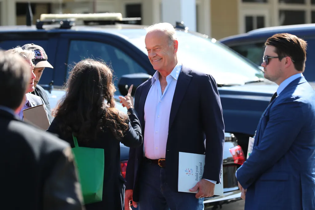 Kelsey Grammer, smiling, holding a folder, stands between a woman and Scott Bessent at the Trump Accounts launch.