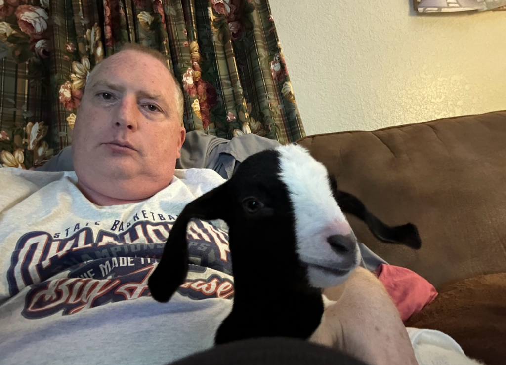 A man relaxing in a chair with a goat standing in front of him