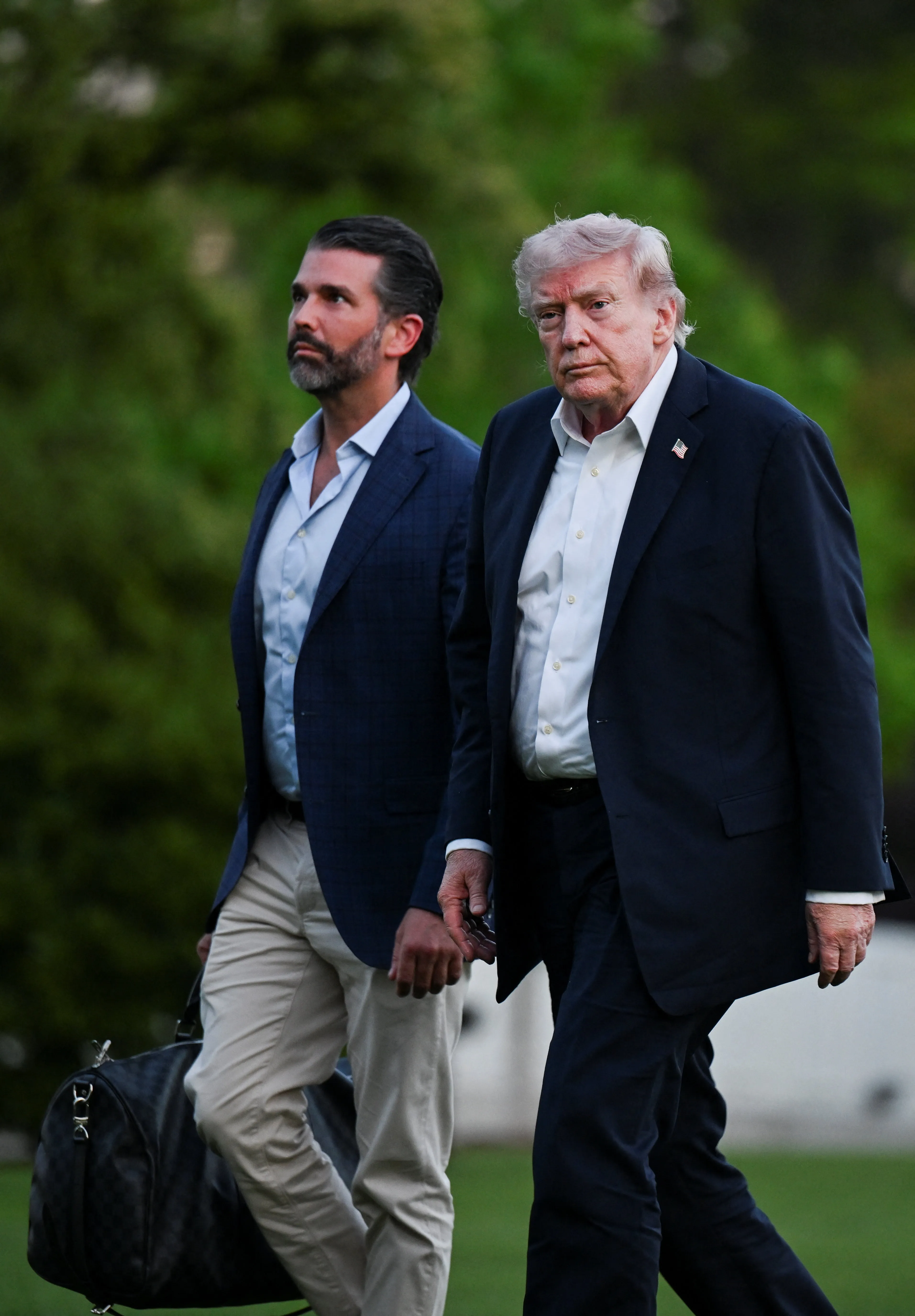 Donald Trump and his son Donald Trump Jr. walking side-by-side with a blurred green background.