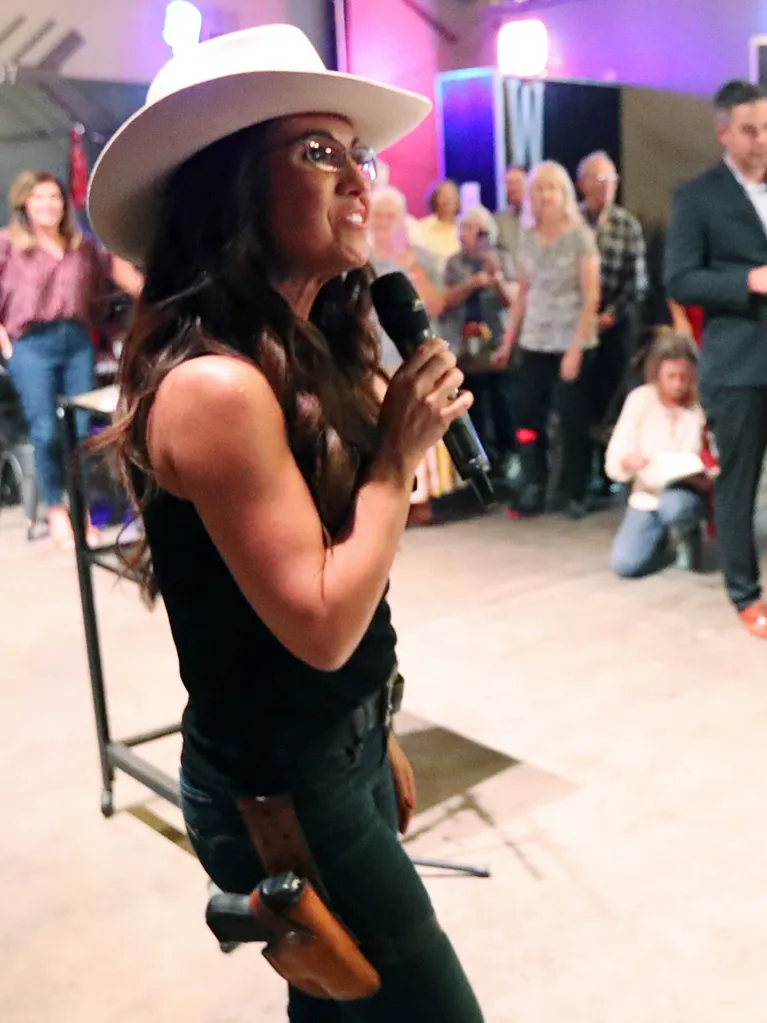 U.S. Rep. Lauren Boebert speaks into a microphone while wearing a cowboy hat and a holstered handgun on her hip during an event.