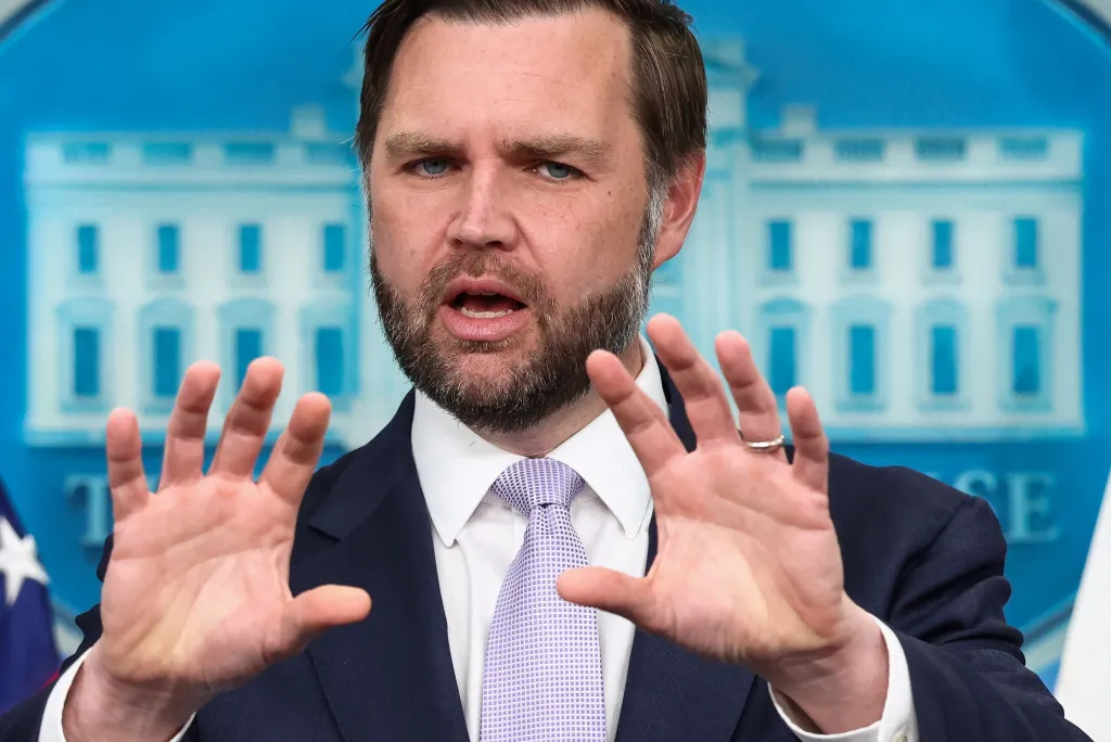 U.S. Vice President JD Vance speaking at a press briefing at the White House, with hands raised, palms out.