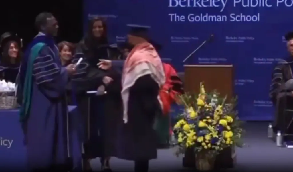 A graduate being stopped by an official at a commencement ceremony while wearing a Palestinian flag as a scarf.