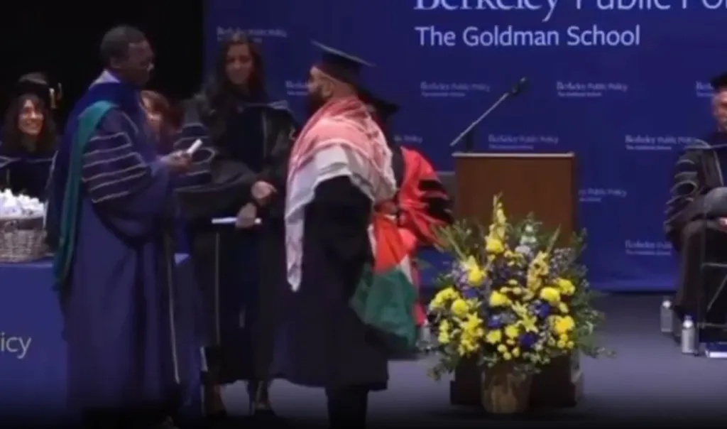 A graduate at UC Berkeley's Goldman School of Public Policy is stopped while wearing a keffiyeh and a Palestinian flag during a graduation ceremony.