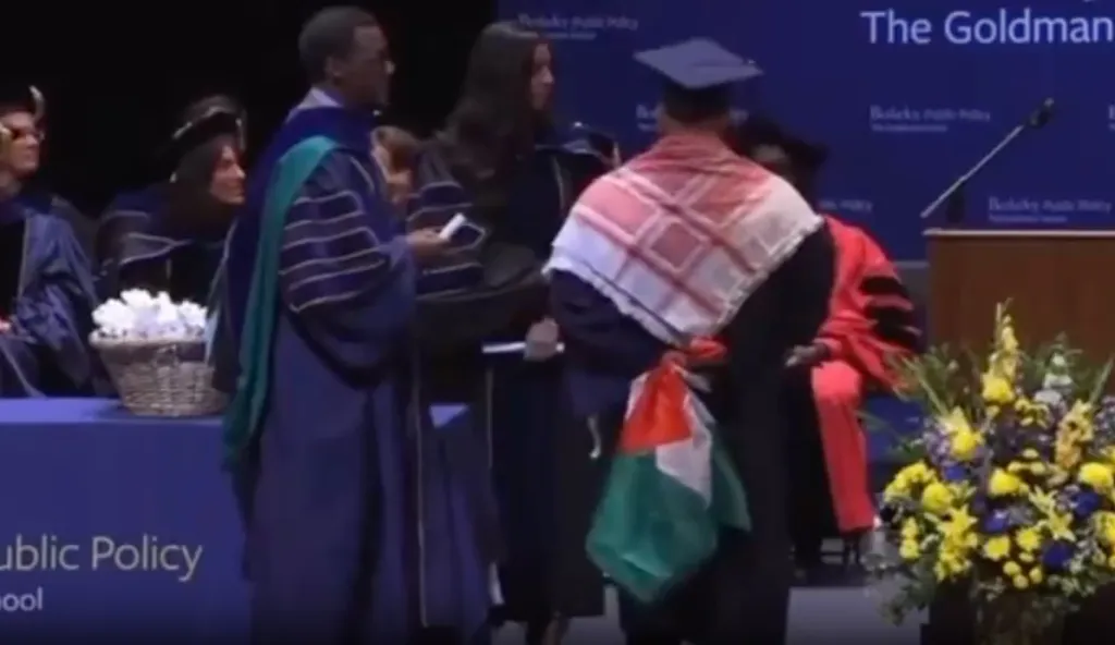 A graduate at UC Berkeley's Goldman School of Public Policy is stopped while wearing a keffiyeh and a Palestinian flag during a graduation ceremony.