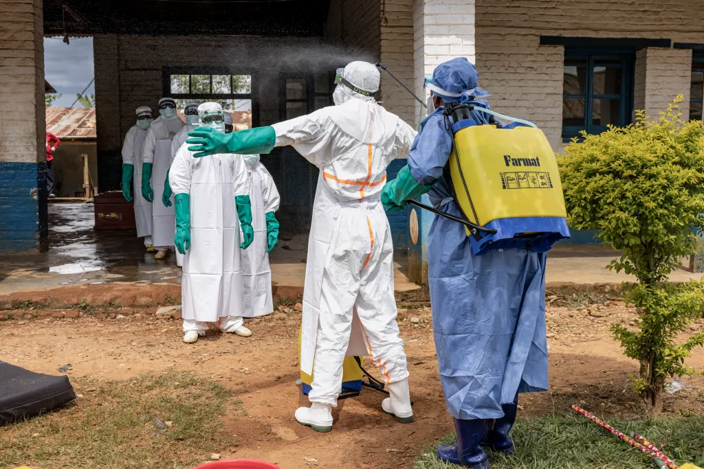 Health workers in protective gear are disinfected after leaving an isolation area during an Ebola outbreak.