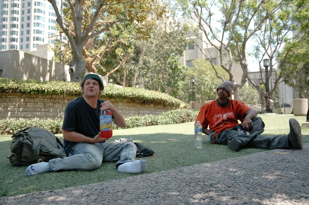 Two unhoused individuals resting on the grass outside the Los Angeles Central Library.