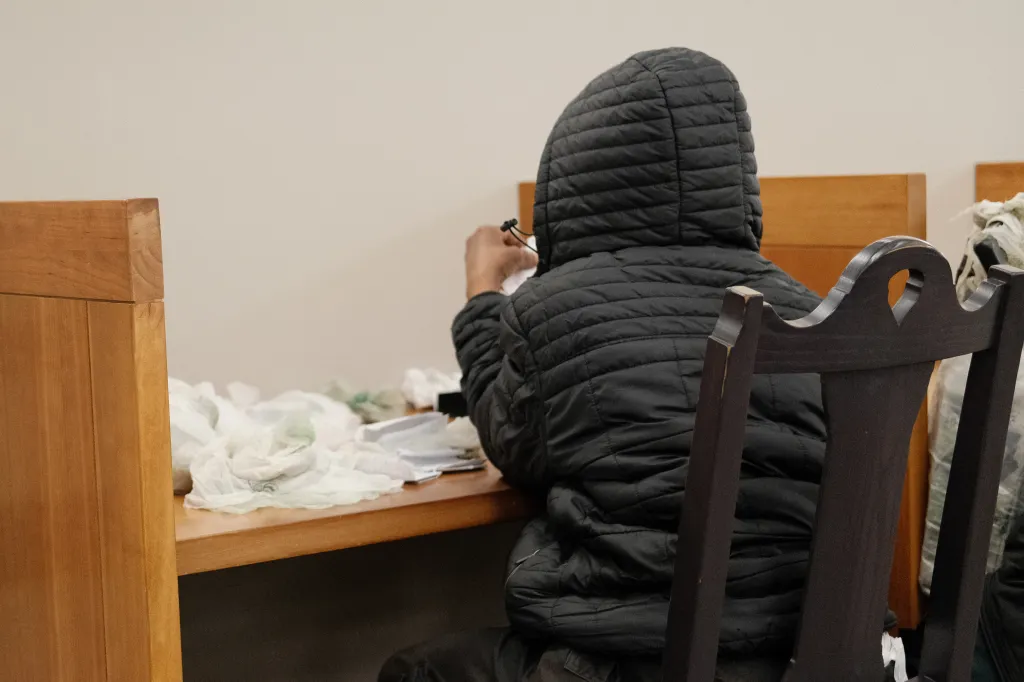 Person in a black hooded jacket at a table covered in plastic bags inside the Los Angeles Central Library.