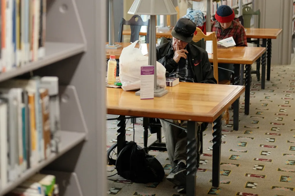An unhoused man and another individual sitting at tables inside the Los Angeles Central Library.