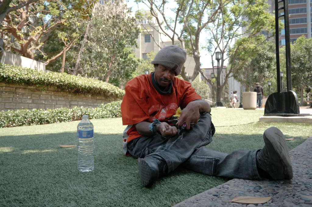 A person experiencing homelessness sits on artificial grass outside the Los Angeles Central Library.