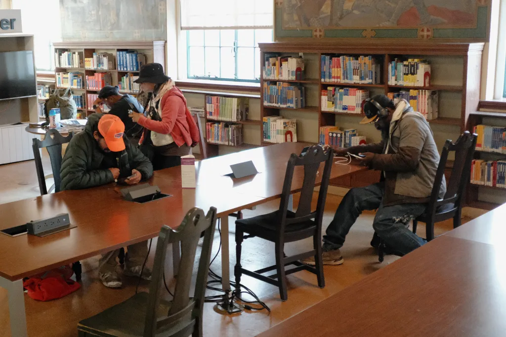 People sitting at tables and charging phones inside the Los Angeles Central Library.