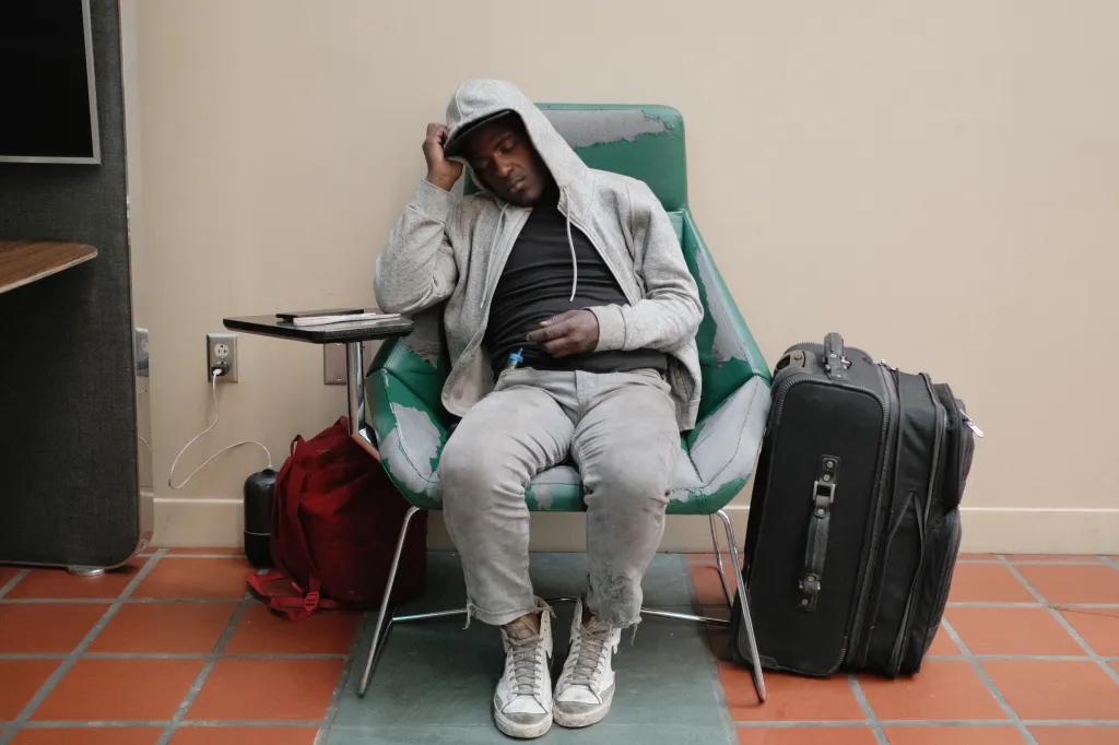 An unhoused man sleeps in a tattered green chair next to his belongings in the Los Angeles Central Library.