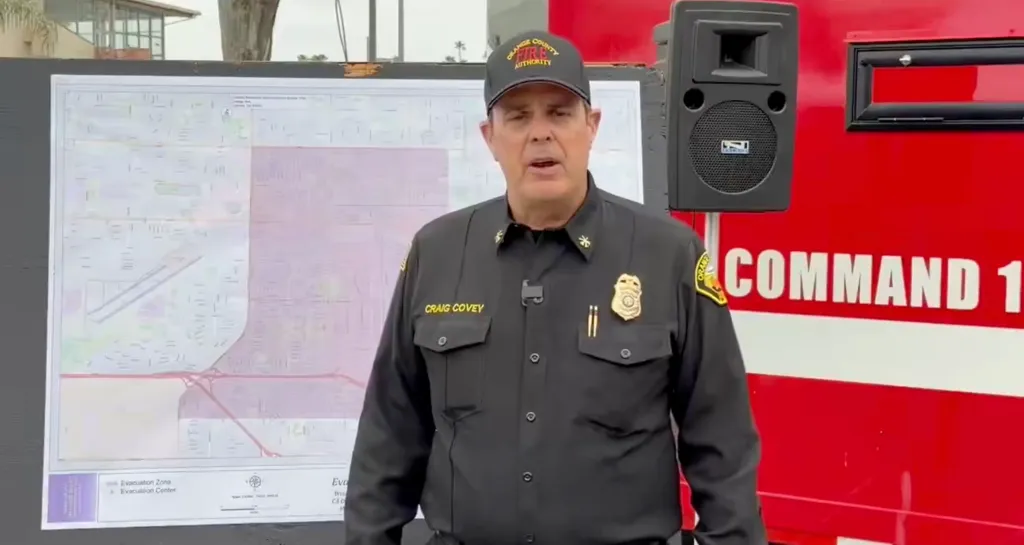 Unified Incident Commander Craig Covey delivering an update in front of a map and a red truck.