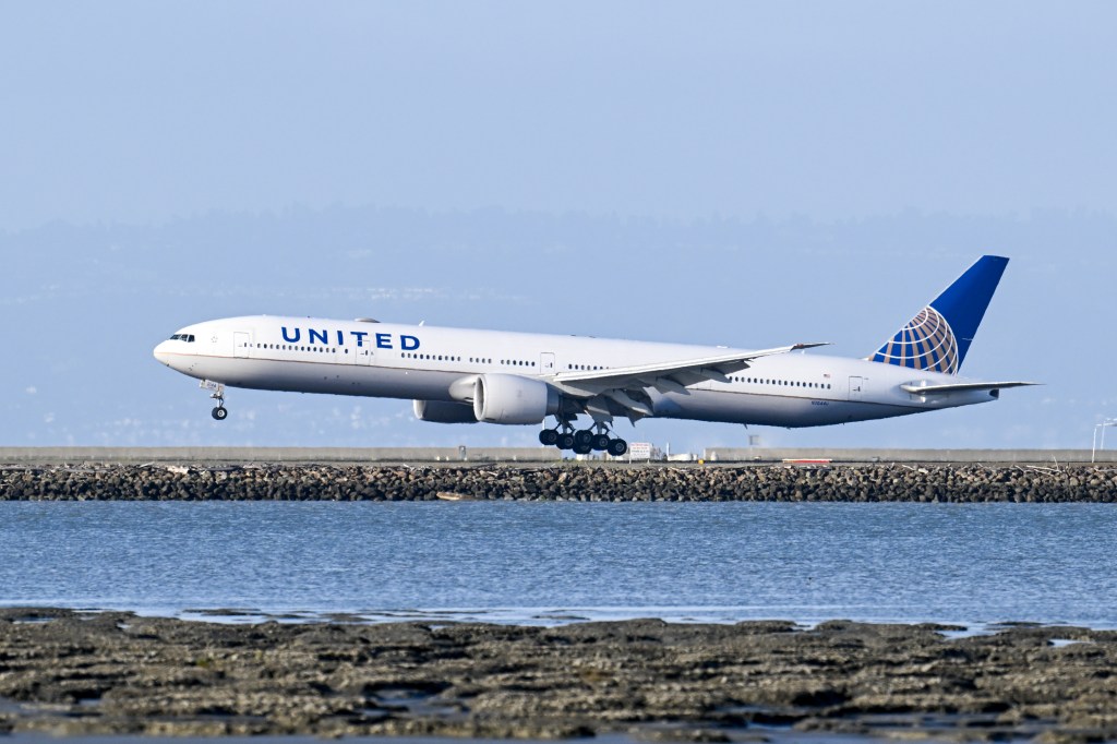 A United Airlines plane descending over water to land at San Francisco International Airport.
