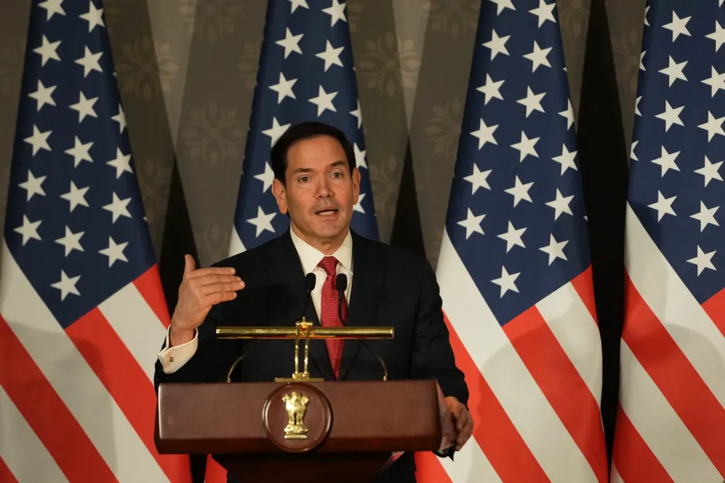 Marco Rubio speaking at a press conference with US flags behind him.