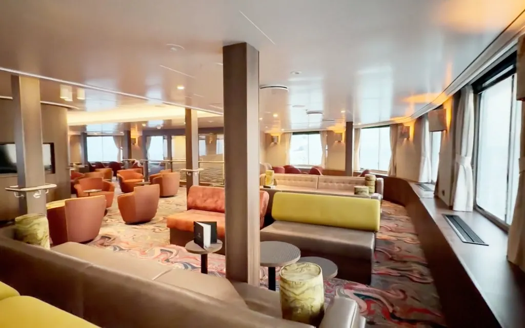 The lounge area inside the MV Hondius cruise ship, with various seating arrangements and large windows.
