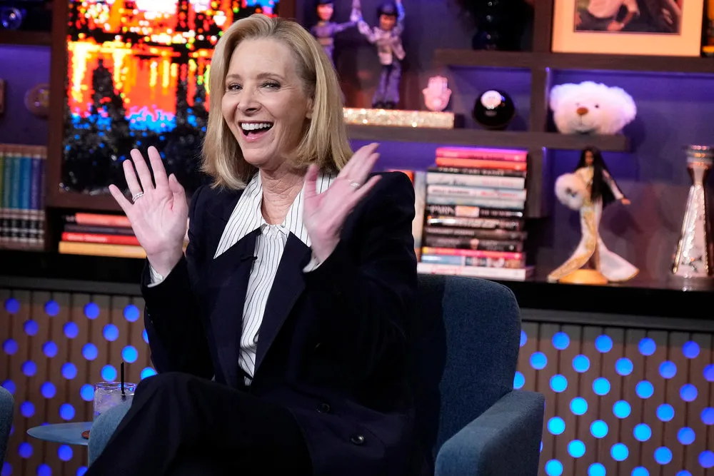 Lisa Kudrow laughing and gesturing with her hands while seated in a studio.