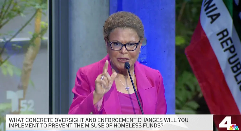 Karen Bass speaks into a microphone, gesturing with her right hand during a mayoral debate.