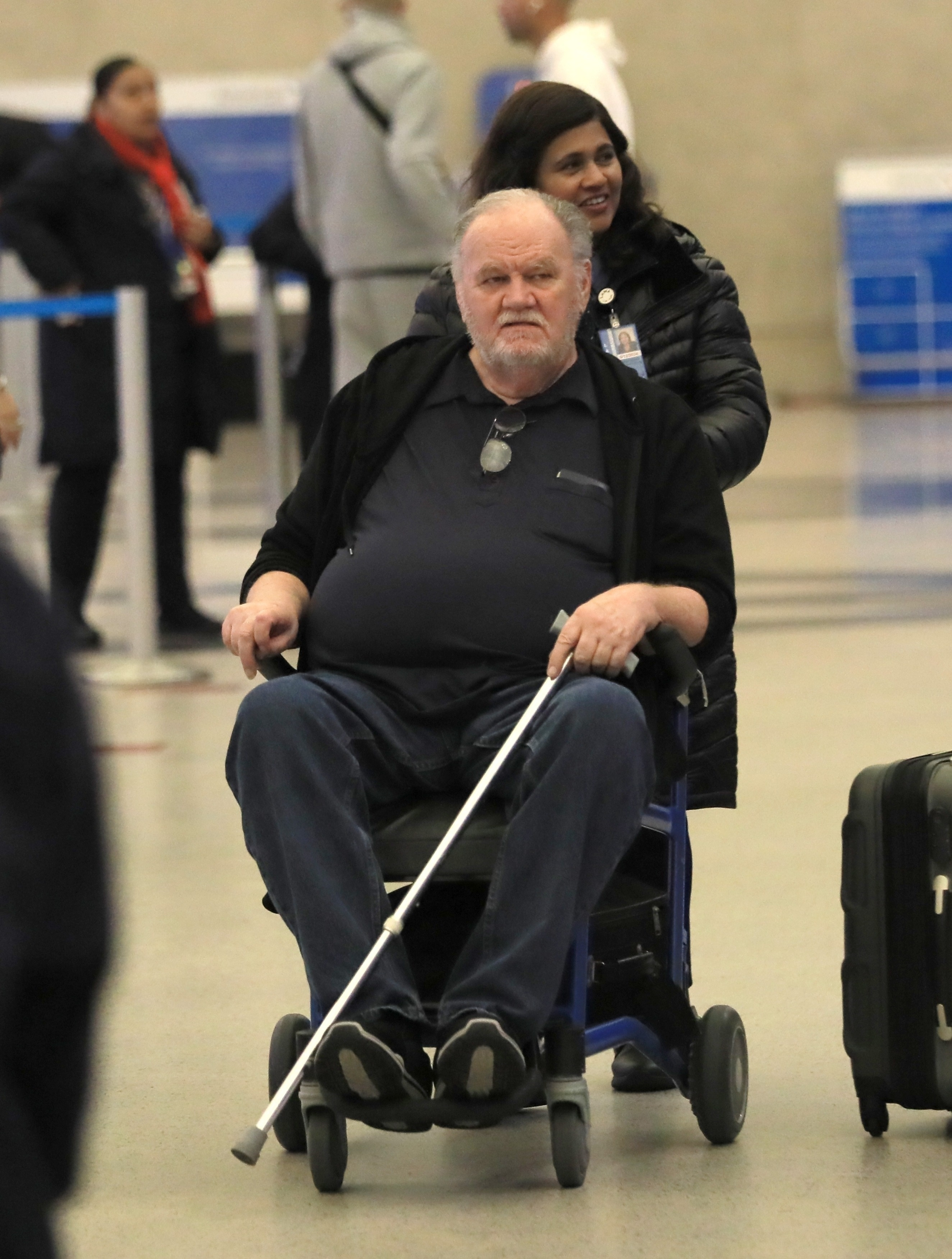 Thomas Markle in a wheelchair, holding a cane, being pushed by a woman.