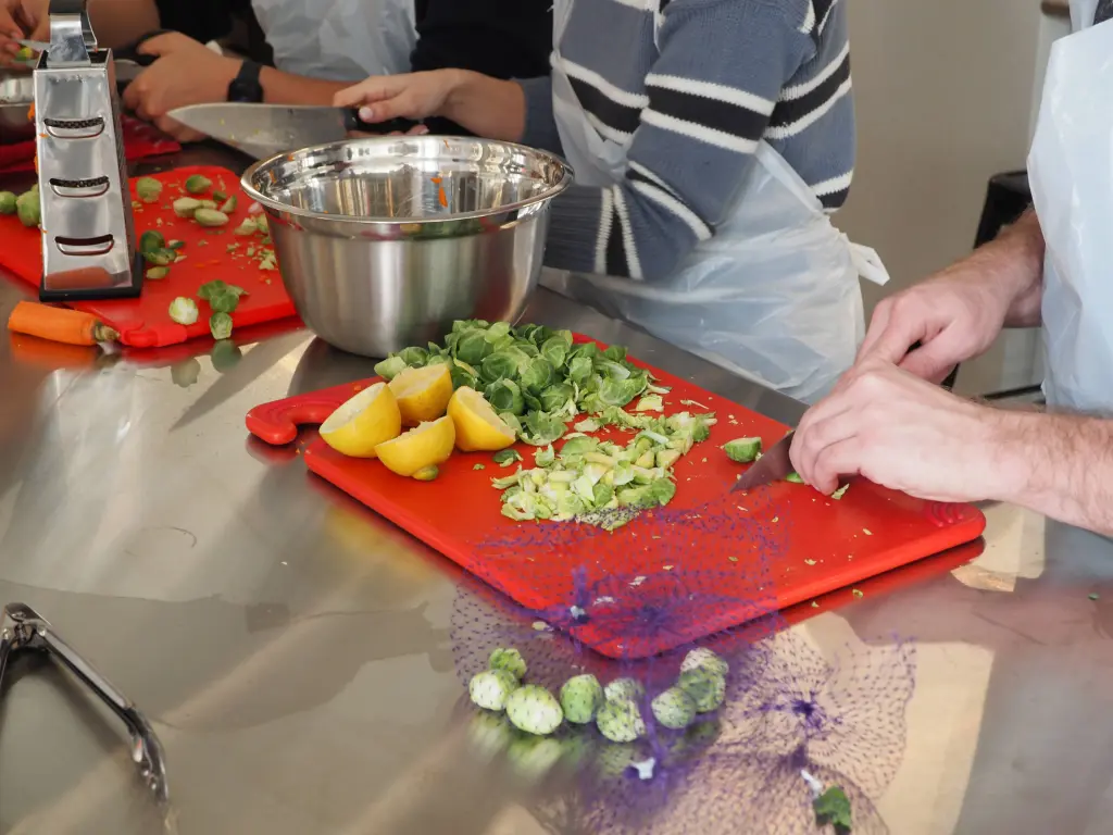 People chopping vegetables and fruit on a red cutting board.