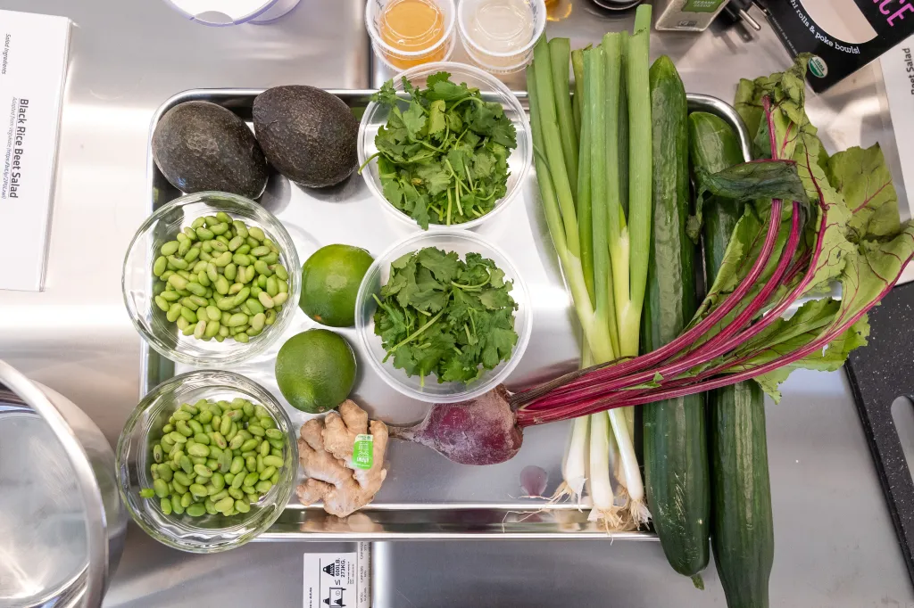 Ingredients for Black Rice Beet Salad, including edamame, avocados, limes, cilantro, ginger, green onions, cucumbers, and beets, laid out on a metal tray.