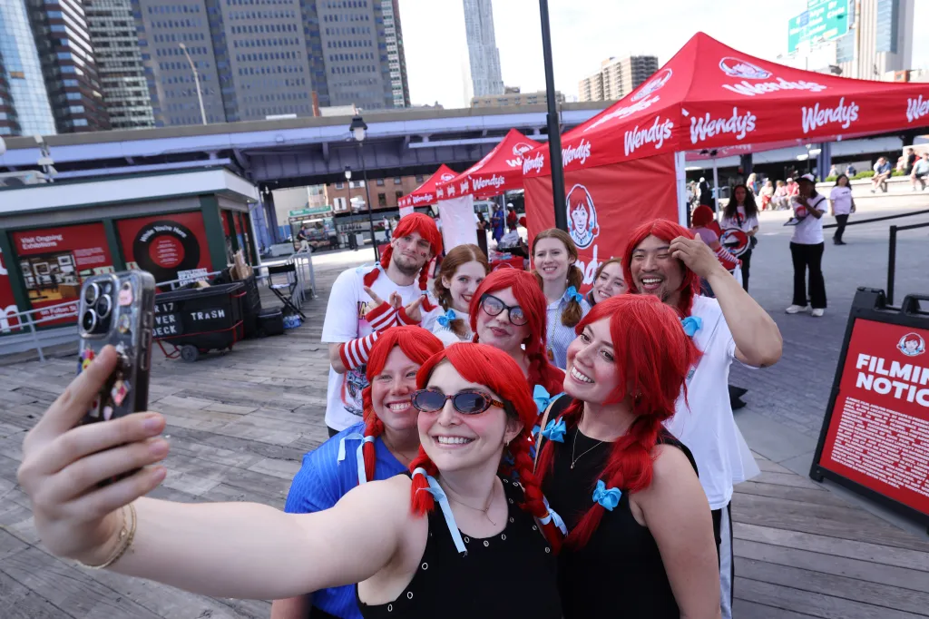 People dressed as Wendy from the Wendy's logo pose for a selfie at an event.