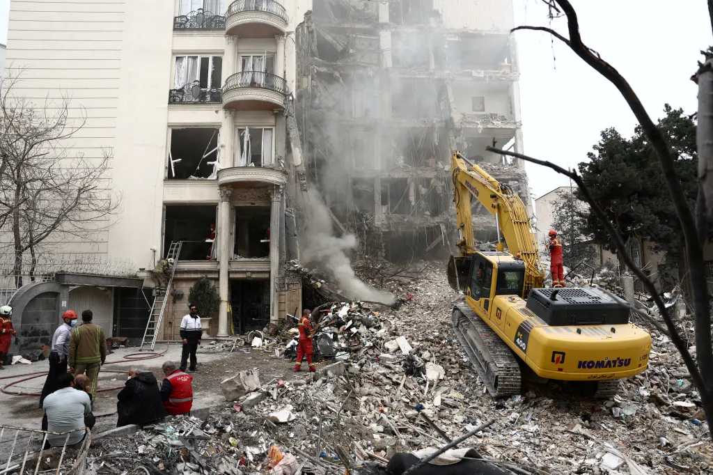 Residential building damaged by a strike in Tehran, Iran, with smoke rising from debris and an excavator among the rubble.