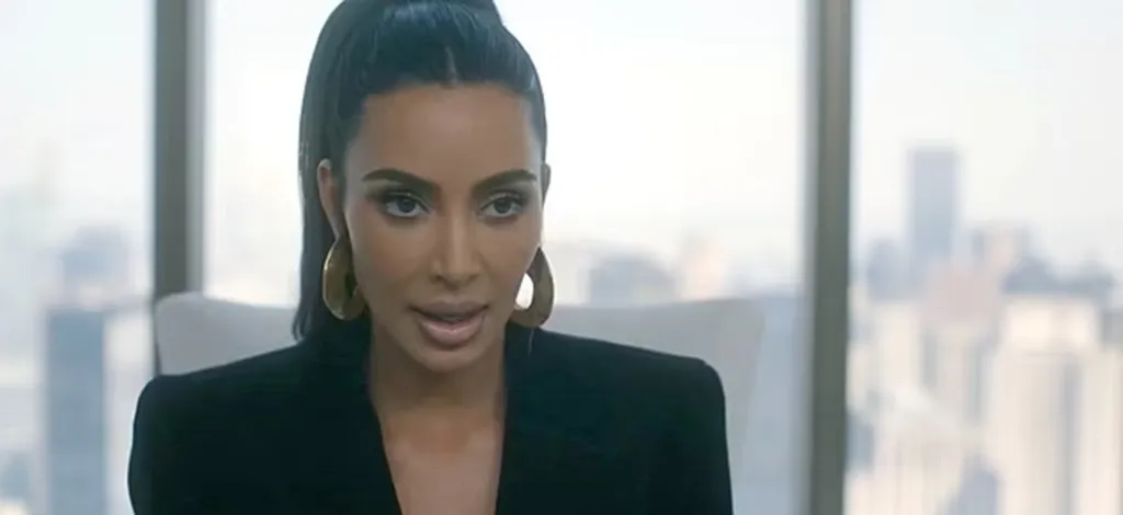 Kim Kardashian speaking, wearing large gold hoop earrings and a black blazer.