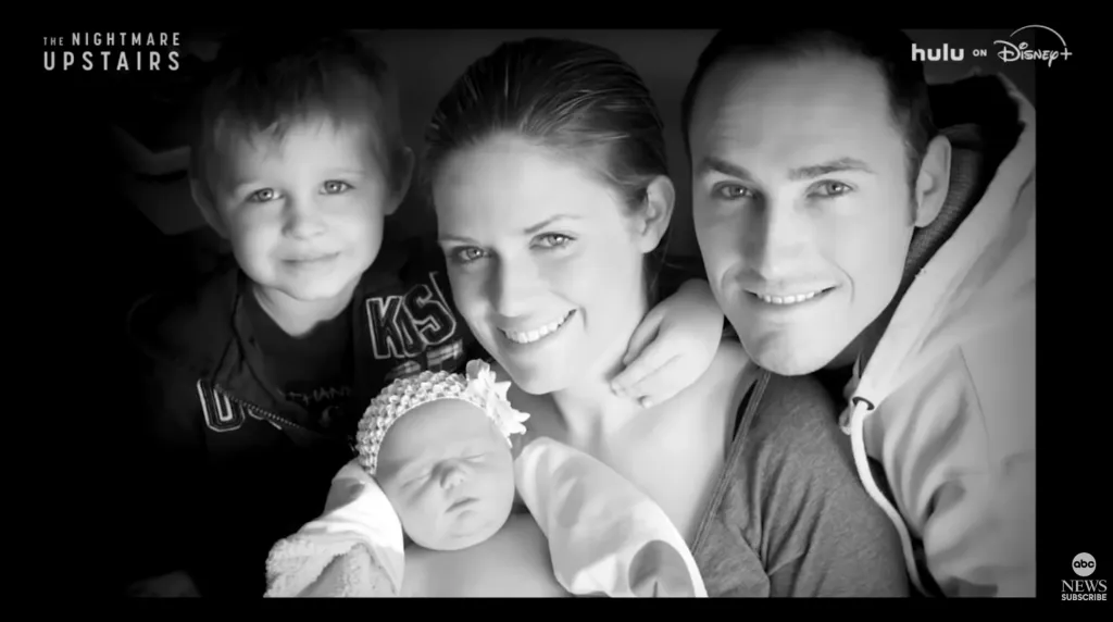 Black and white photo of a smiling family of four, including two parents, a young boy, and an infant.