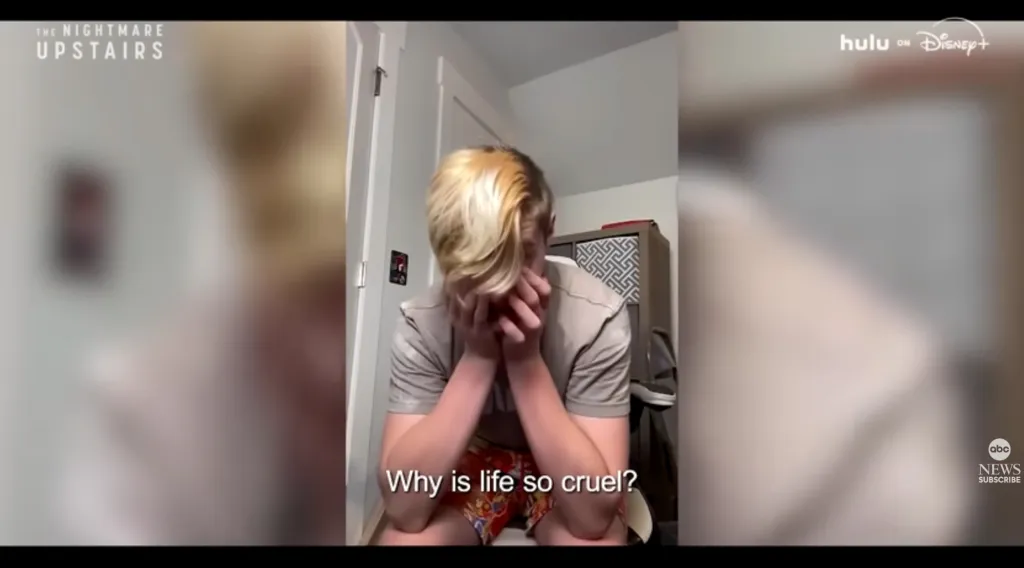 A young person with bleached blonde hair sitting down, covering their face with their hands, with the text 
