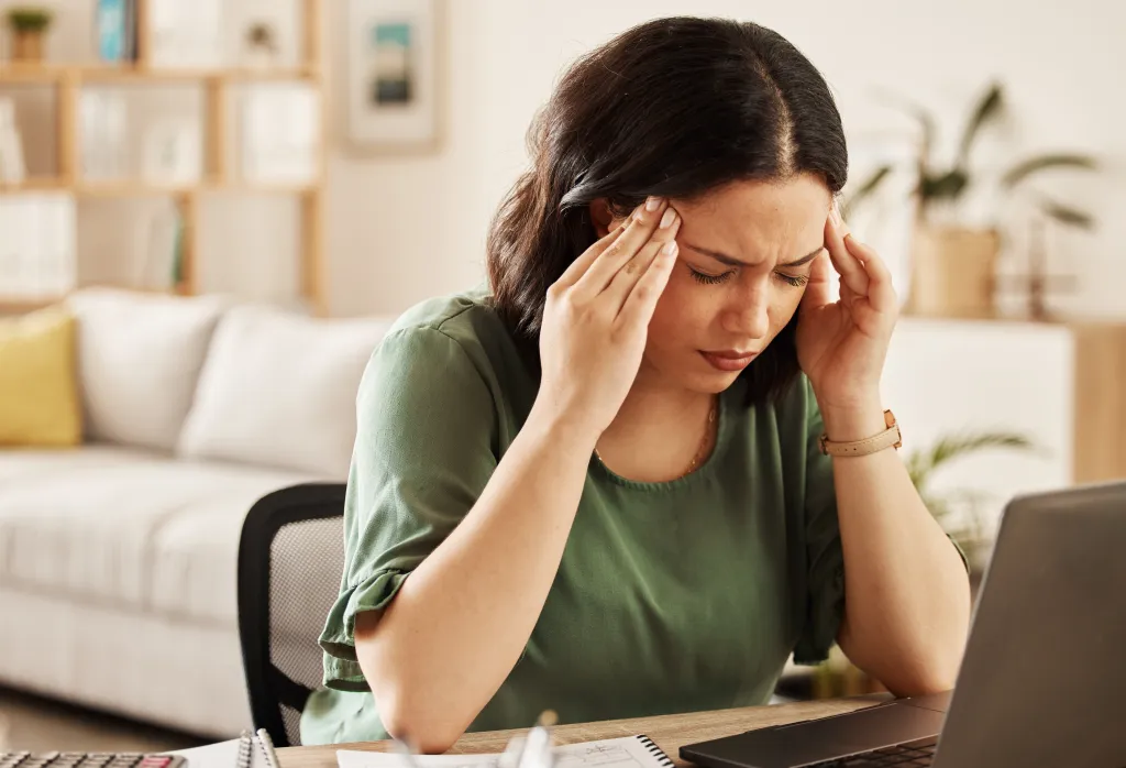 Woman experiencing burnout and a headache while working remotely on her laptop.