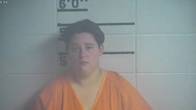 Mugshot of Brook Ann McDaniel, a woman with dark hair and an orange shirt, standing in front of a height chart.