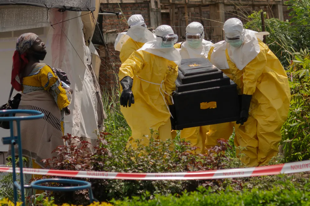 A woman watches as Red Cross workers in yellow protective suits carry a coffin.