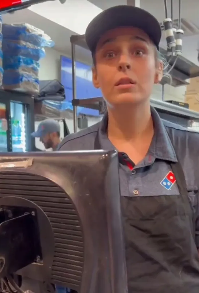 Domino's employee wearing a uniform and a hat, looking surprised.