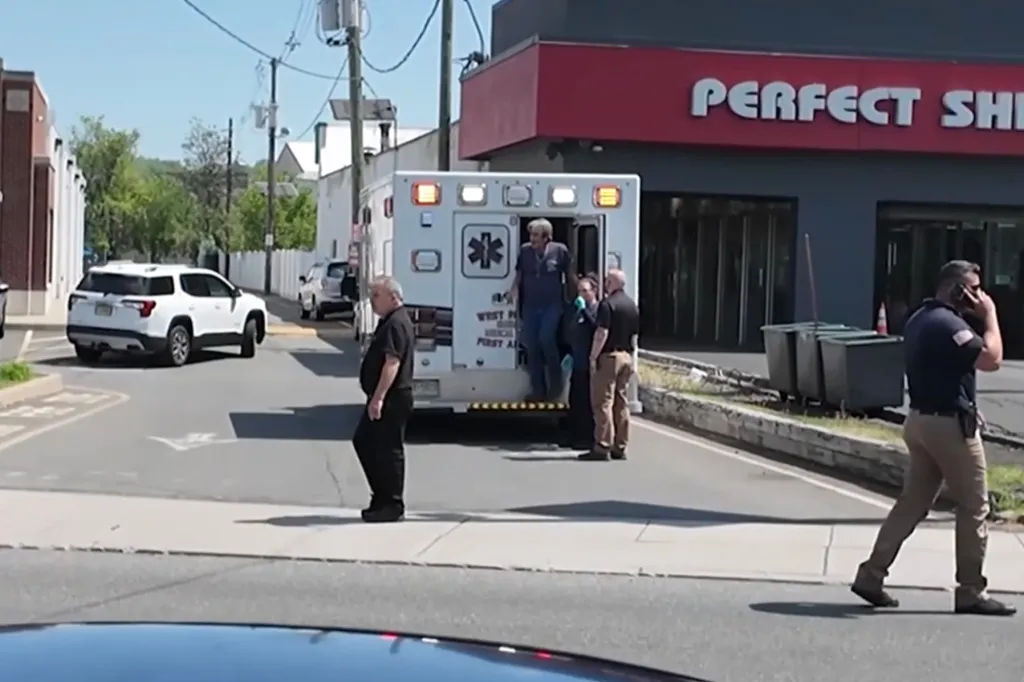Ambulance with its back door open with medical personnel and a civilian standing around it on the street.