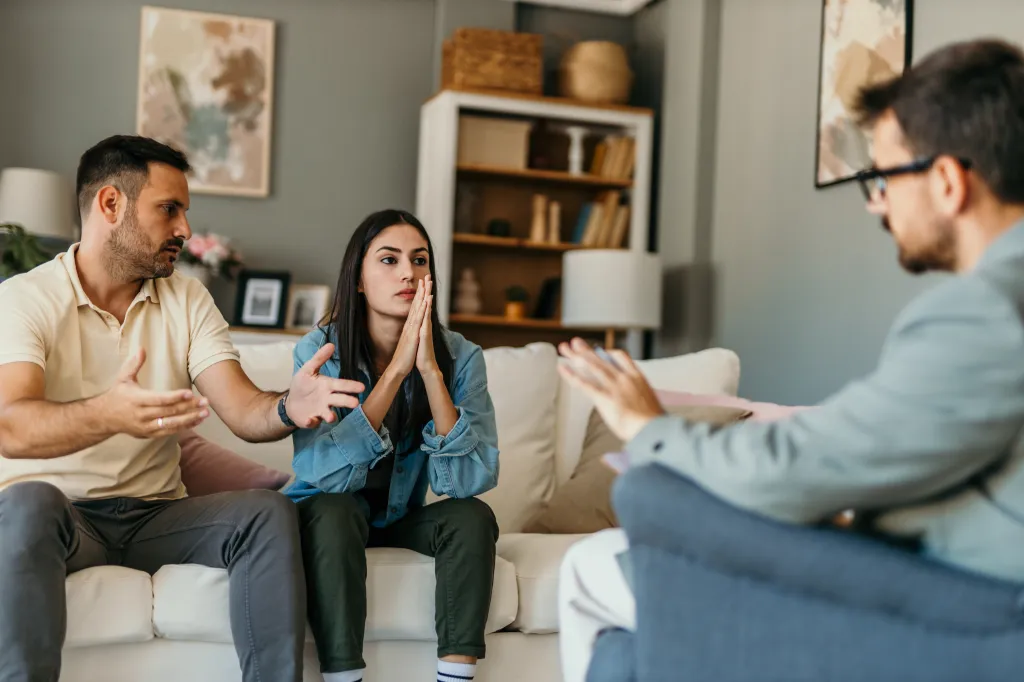 Young couple arguing during a therapy session with a male psychologist.