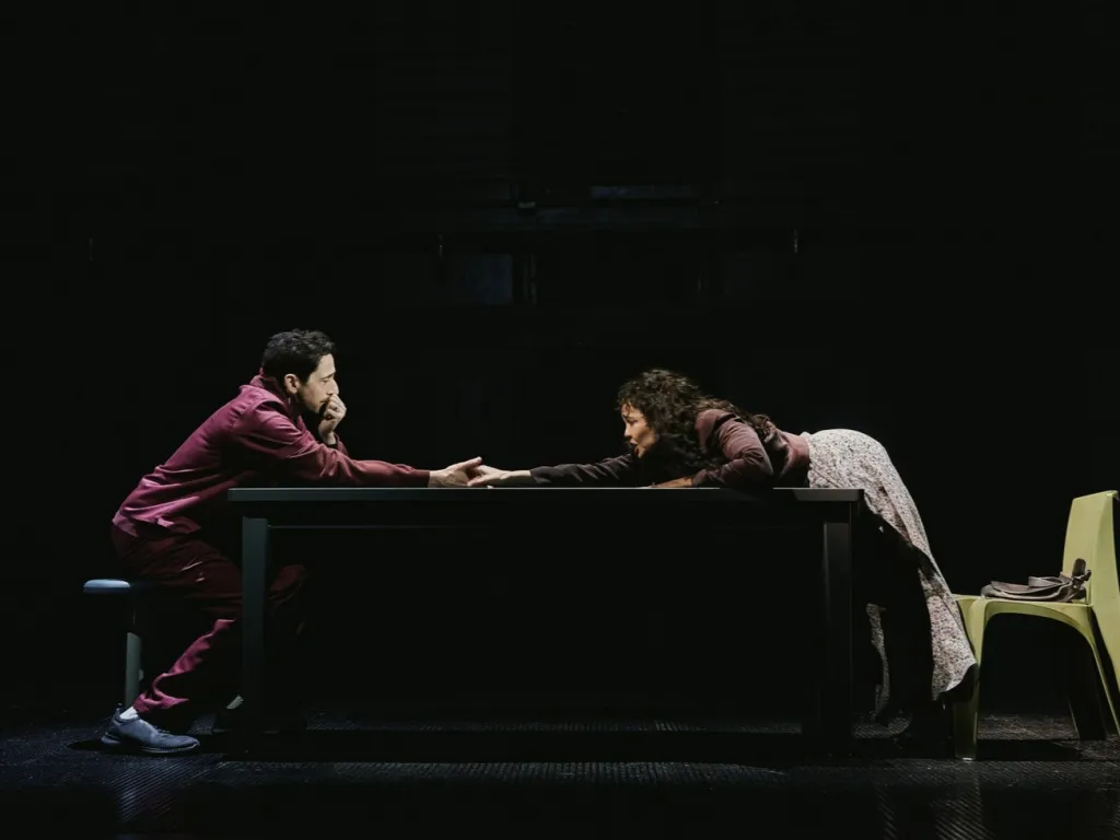 Adrien Brody and Tessa Thompson reaching for each other's hands across a table.
