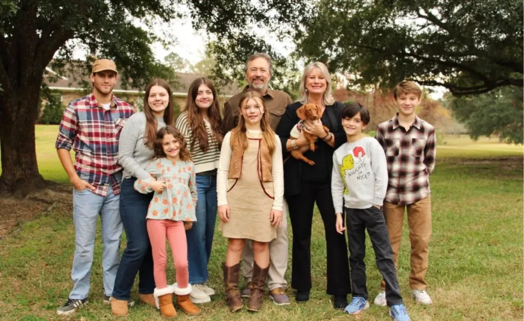 Al and Lisa Robertson pose outdoors with their large family, including children, grandchildren, and a dog.