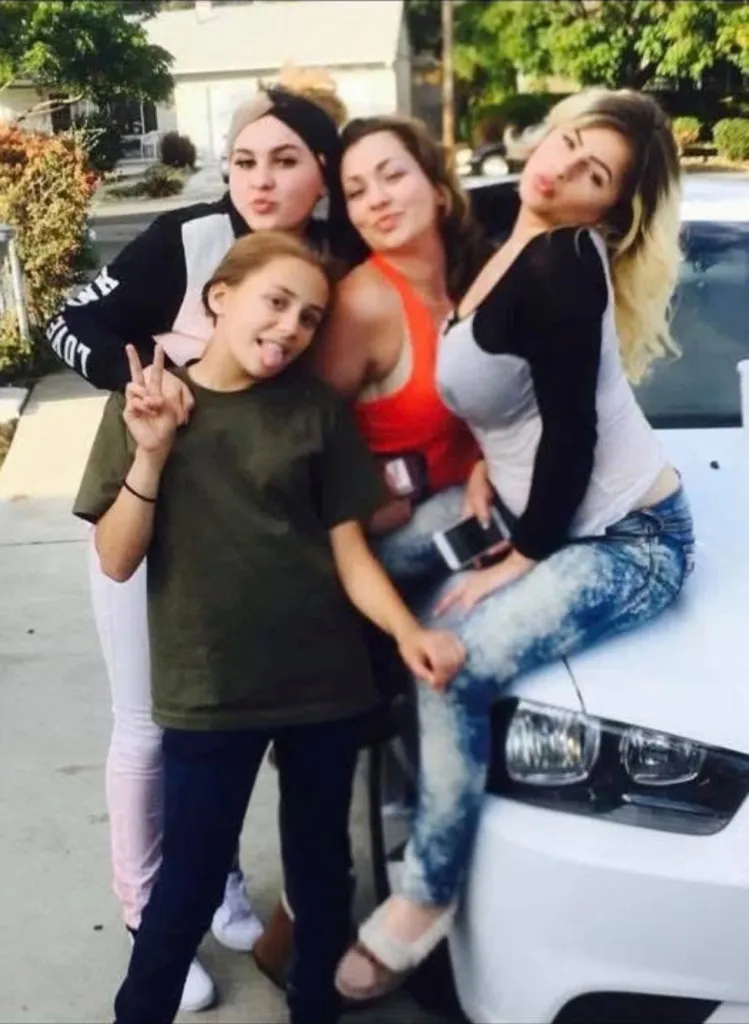 Four women posing for a picture in front of a white car.
