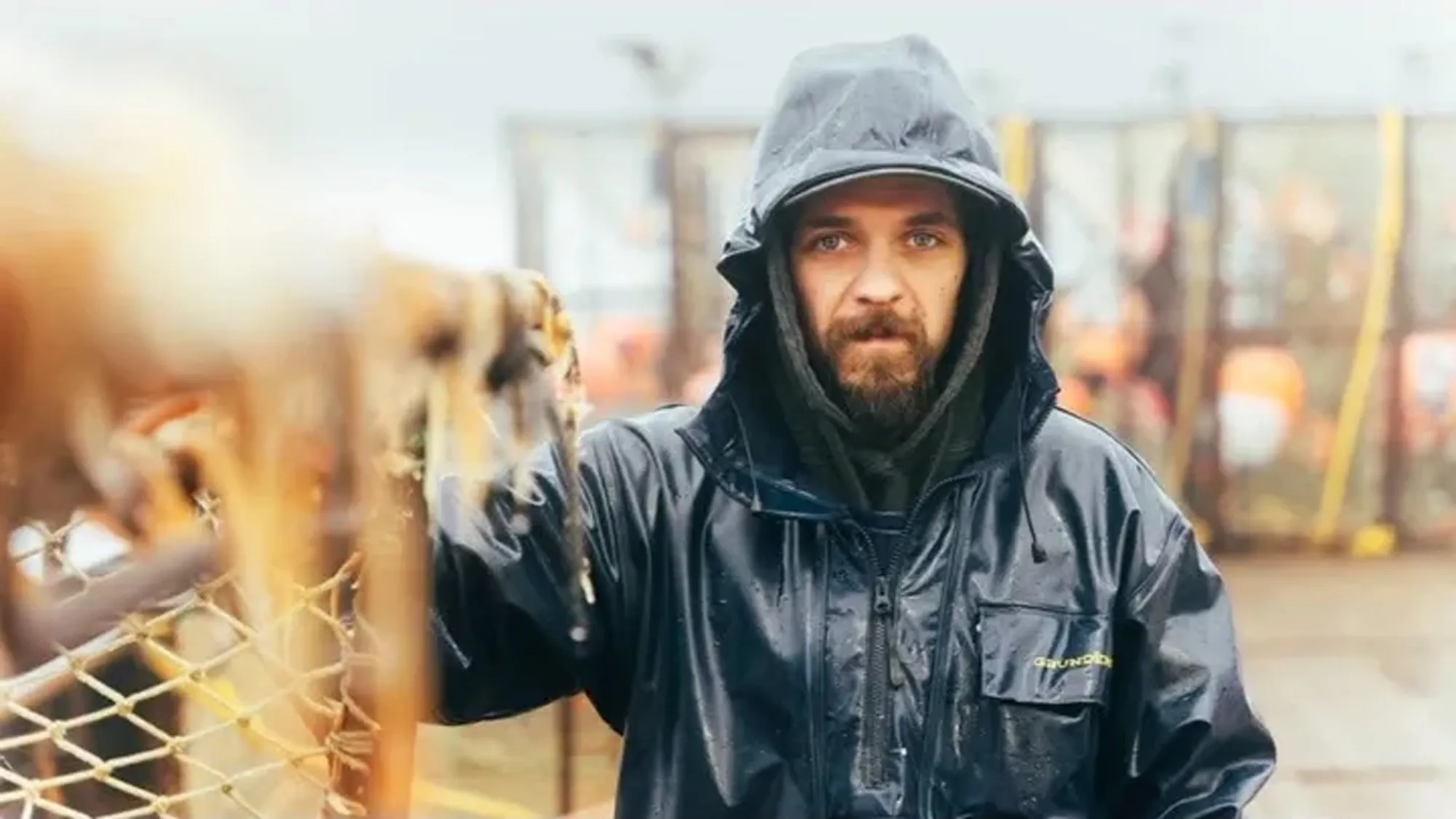 Todd Meadows, a man with a beard and hooded rain jacket, stands on a boat with fishing equipment.