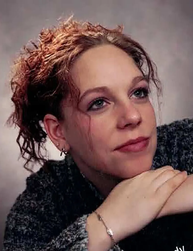 Brandy Gail Phillippe, a woman with reddish-brown curly hair, wearing a dark gray sweater and a silver bracelet, rests her chin on her hands and looks upward.