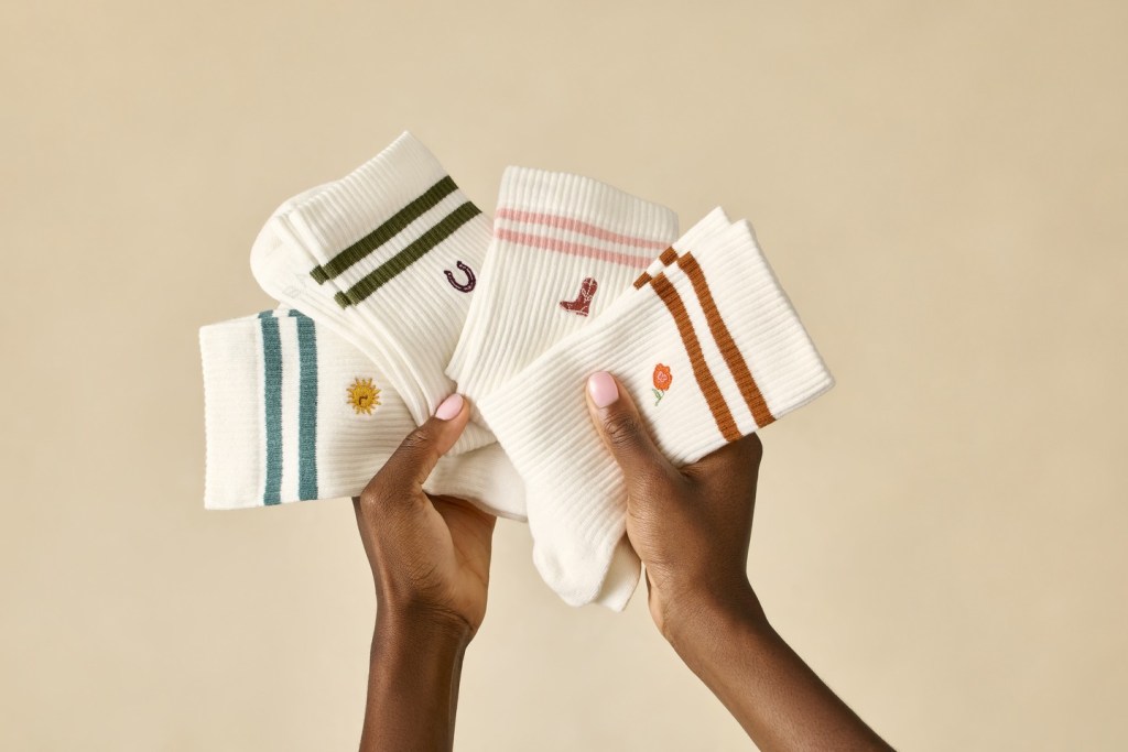 Hands holding Bombas socks with embroidered designs.