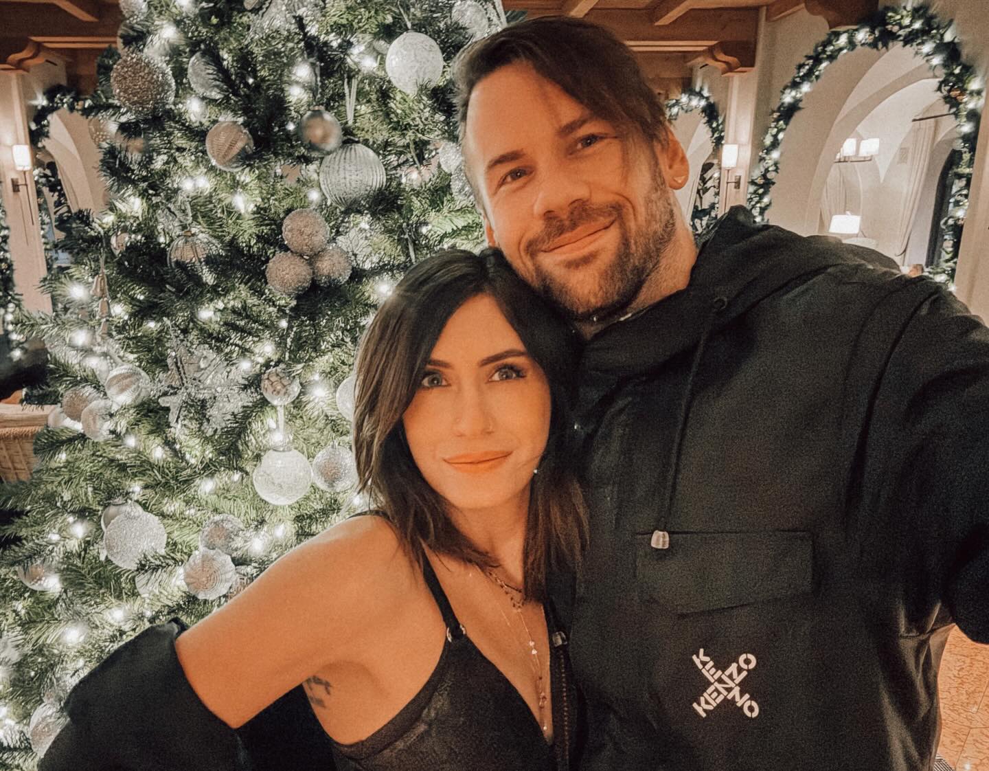 Caleb Shomo and his wife in front of a Christmas tree.