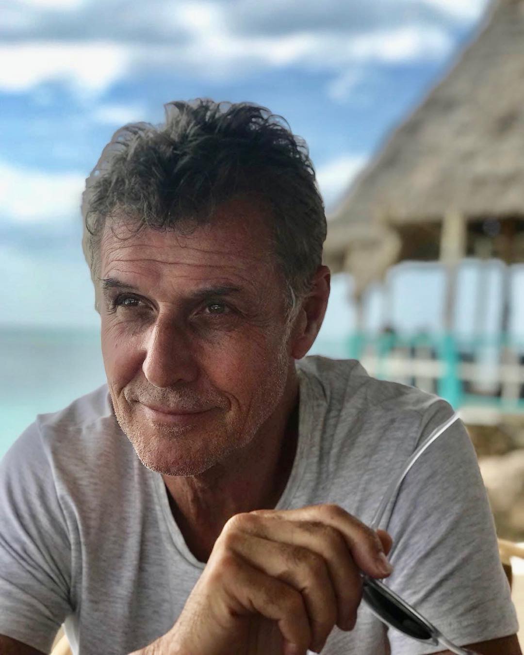 Deny, a man with graying hair, smiling with an ocean background.