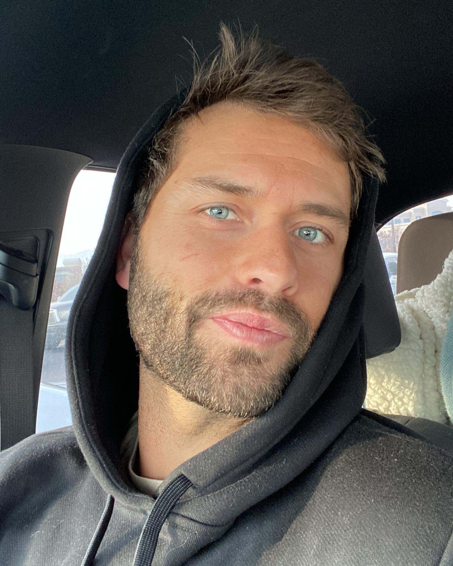 Man with a beard and light blue eyes wearing a black hoodie.