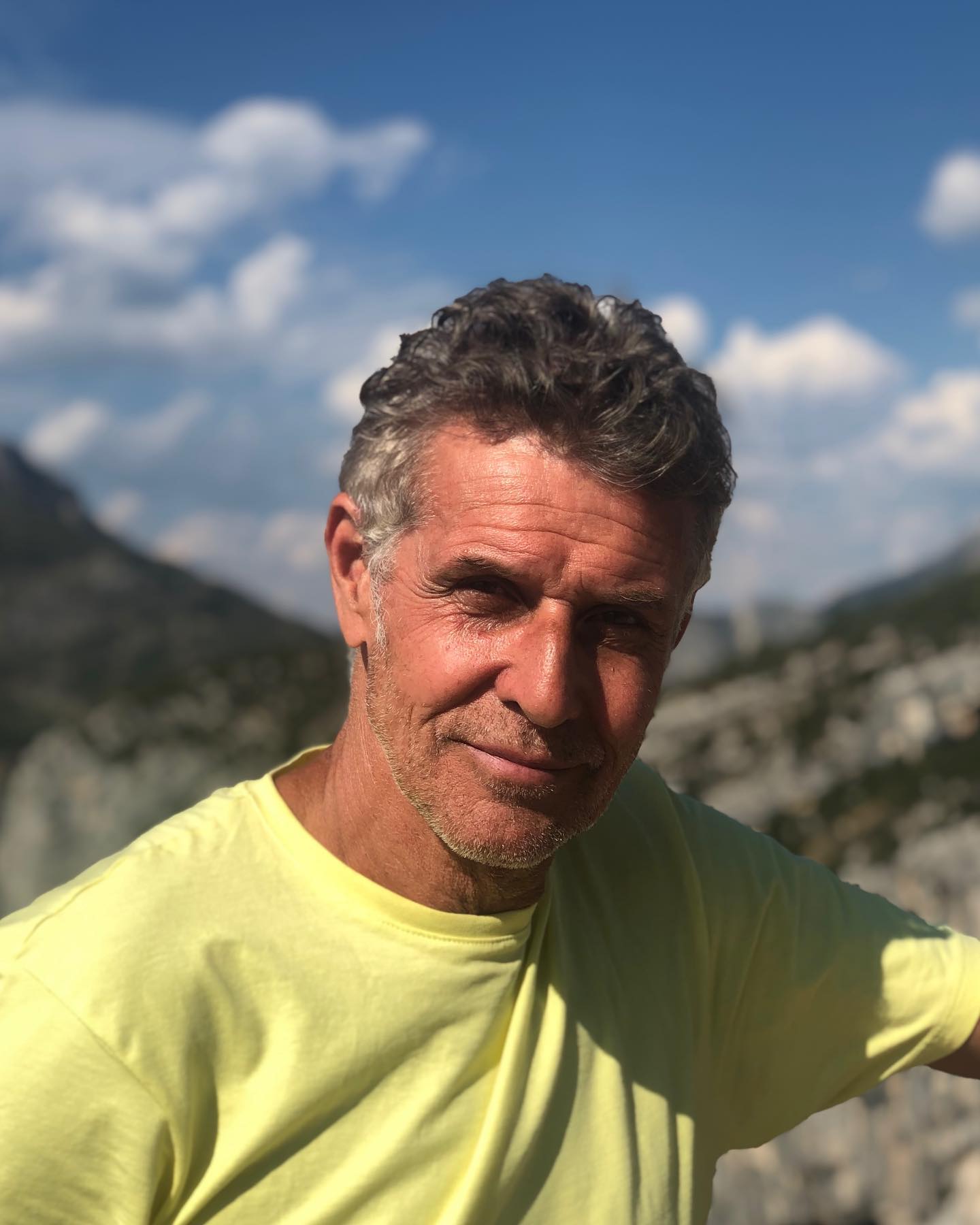 Actor Kirby Morrow smiling with a mountainous background.