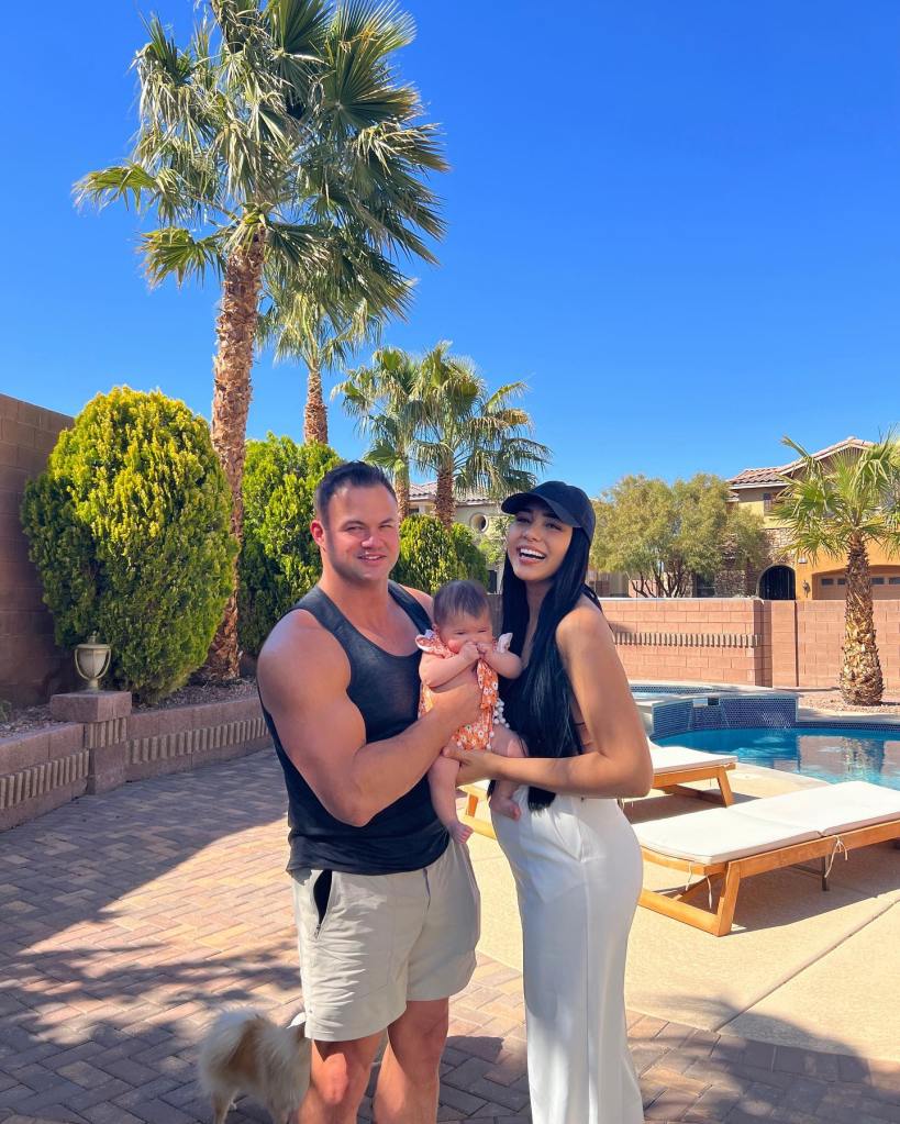90 Day Fiancé' stars Patrick Mendes and Thais Ramone holding their baby, with a dog by their feet, next to a pool.
