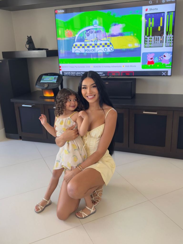 Thais Ramone with her daughter in front of a TV displaying Peppa Pig.
