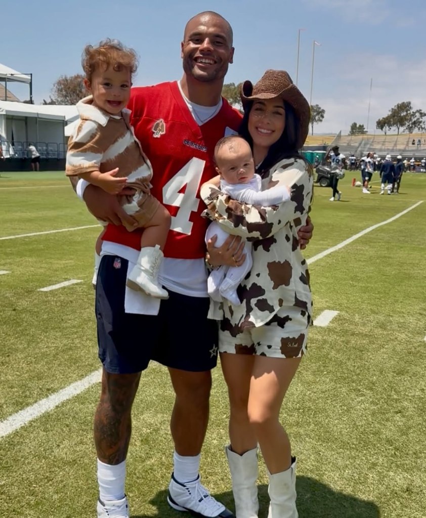 A family of four, including a man in a red Cowboys jersey, a woman in a cowboy hat and cow print outfit, and two young children.