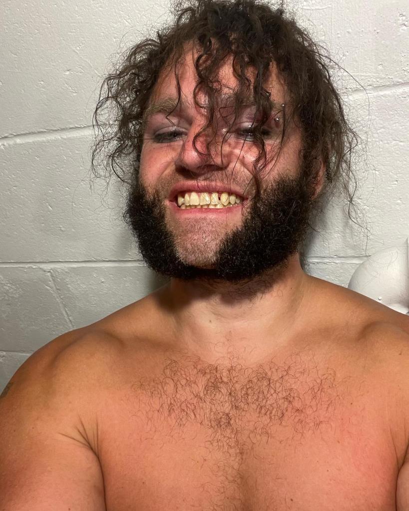 Gabe Brown with messy hair, a beard, and chest hair, smiling at the camera.