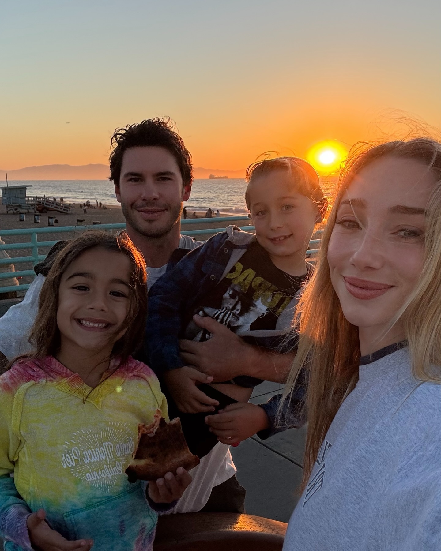 Family of four on a pier at sunset with the ocean and beach in the background.